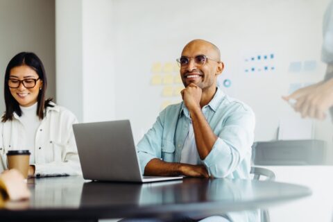 Business man listening to a discussion during a meeting with his team. Happy young designer sitting at a table with his colleagues in a creative office.