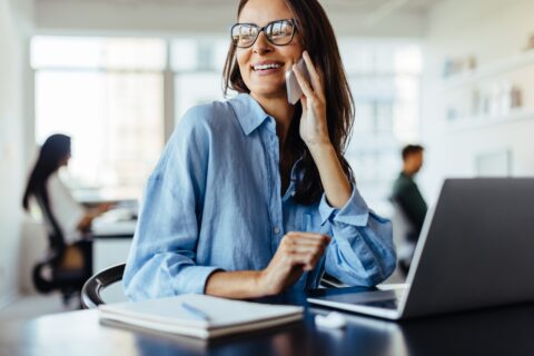 Female business professional making a phone call while sitting in an office. Business woman working with a laptop in a co-working office.
